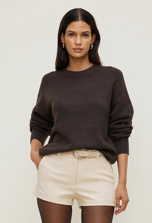 Model is wearing a brown crewneck sweater and beige mini shorts.