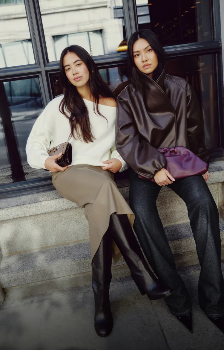 Model on the left is wearing a brown faux leather cocoon jacket. Model on the right is wearing a white off shoulder sweater.