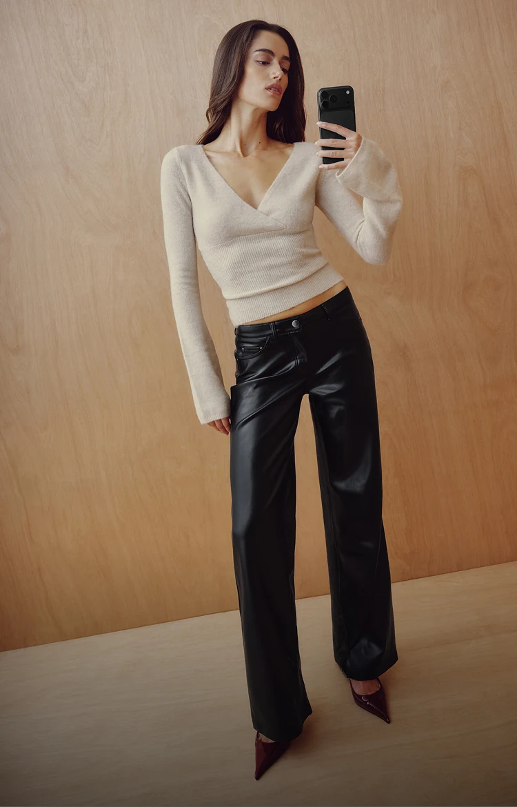 Model is wearing a white plunge sweater and black faux leather pants.