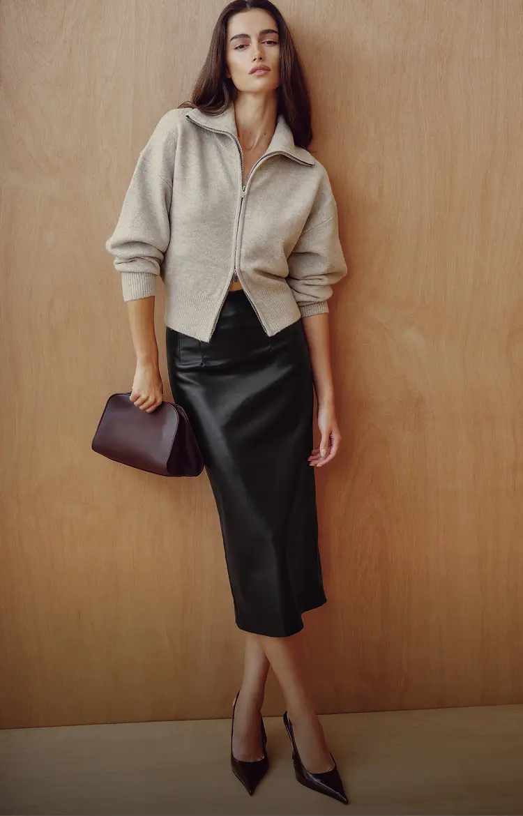 Model is wearing a beige polo cardigan and a black faux leather midi skirt.
