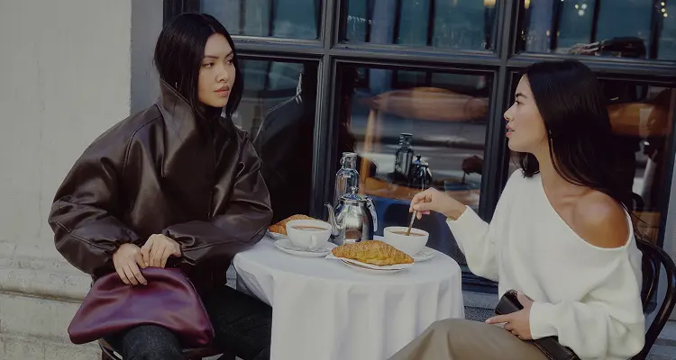 Model on the left is wearing a brown faux leather cocoon jacket. Model on the right is wearing a white off shoulder sweater.