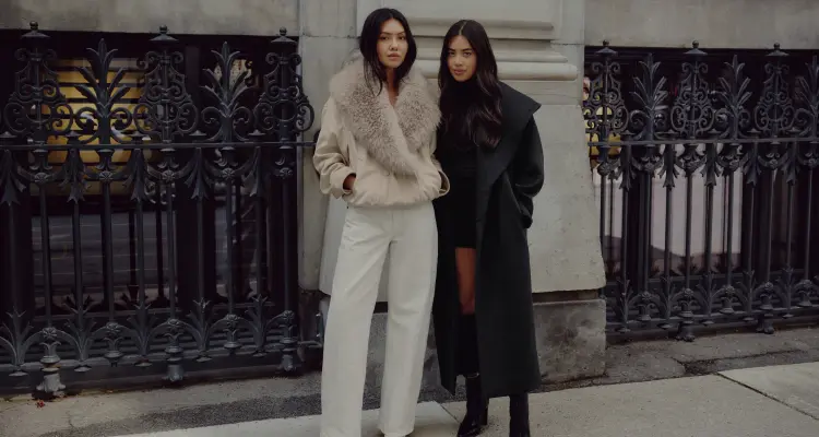 Model on the left is wearing a beige faux fur aviator jacket. Model on the right is wearing a black turtleneck and black woolen coat.