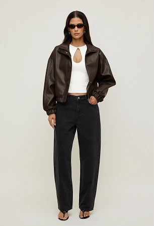 La mannequin porte un blouson aviateur en faux cuir brun par-dessus un haut blanc à ouverture et un jean noir à jambe ballon.
