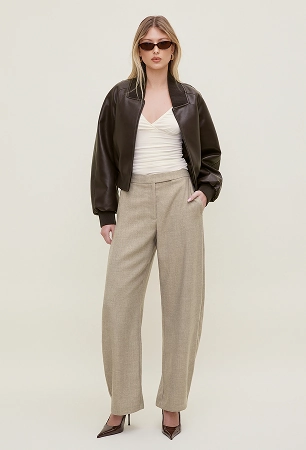 La mannequin porte un blouson aviateur en faux cuir brun par-dessus un haut blanc décolleté et un pantalon beige.