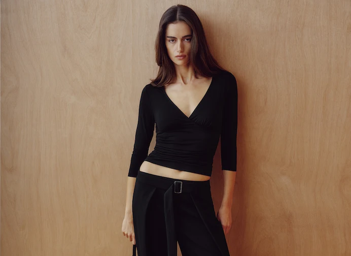 La mannequin porte un haut noir à manches 3/4 et un pantalon noir drapé avec une ceinture.