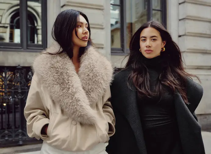 La mannequin de gauche porte un blouson aviateur en fausse fourrure beige. La mannequin de droite porte un col roulé noir et un manteau en laine noir.